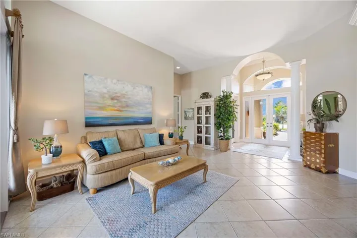 Living room featuring french doors, a high ceiling, light tile patterned flooring, and decorative columns