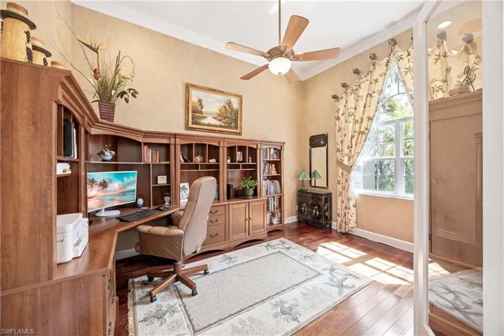 Home office with dark wood-style floors, ceiling fan, baseboards, and crown molding