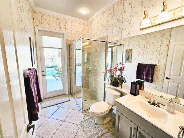 Bathroom with wallpapered walls, ornamental molding, tile patterned floors, vanity, and a shower stall
