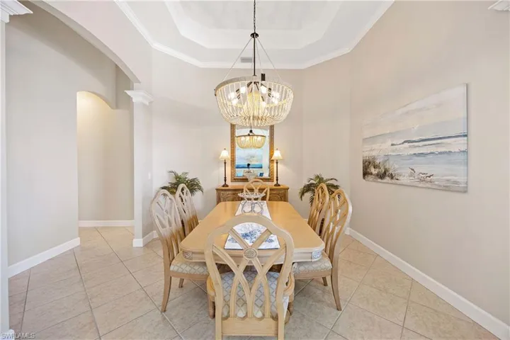 Dining room featuring arched walkways, a raised ceiling, baseboards, and an inviting chandelier
