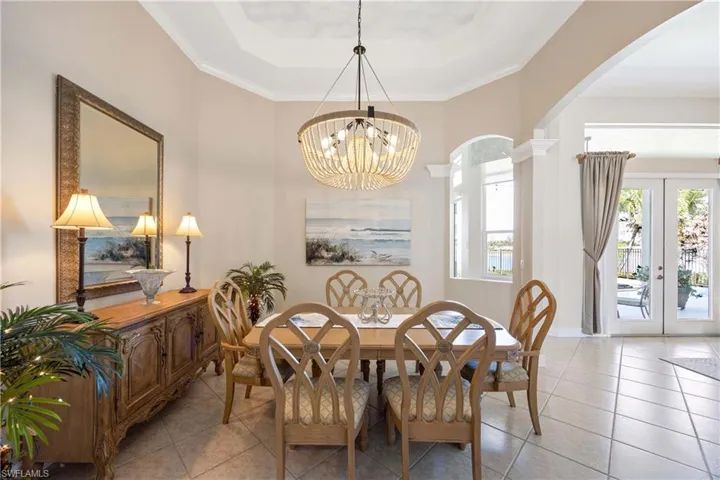 Dining space featuring arched walkways, a tray ceiling, french doors, a notable chandelier, and light tile patterned flooring