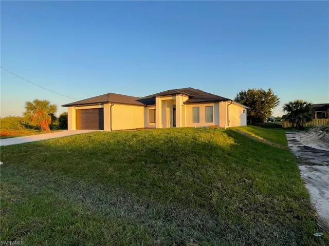 View of front of house with stucco siding, a garage, driveway, and a front lawn