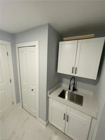 Laundry room featuring a sink, light marble finish flooring, and baseboards