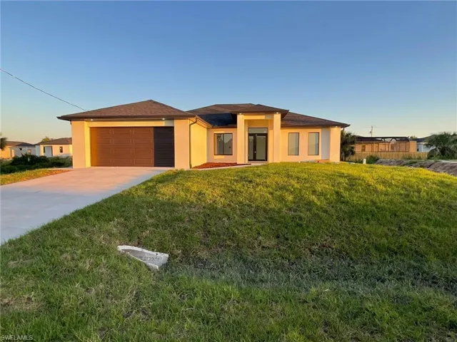 Prairie-style home with a garage, a front lawn, stucco siding, and driveway