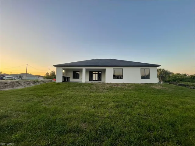 Back of house at dusk featuring a lawn and stucco siding