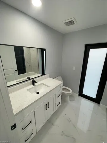 Bathroom featuring marble finish flooring, vanity, toilet, and baseboards