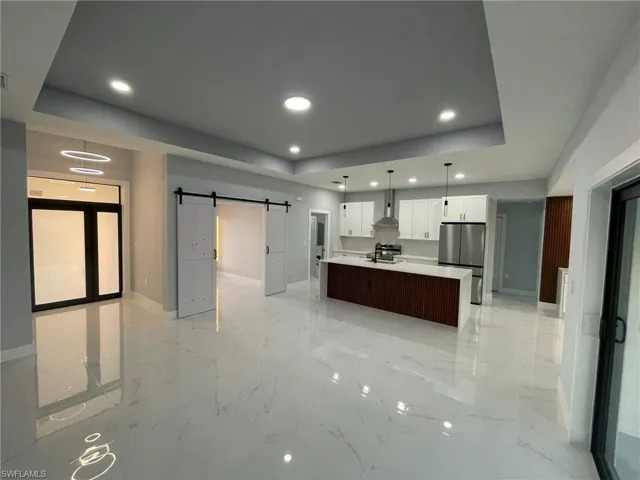 Kitchen featuring freestanding refrigerator, a tray ceiling, a barn door, baseboards, and recessed lighting