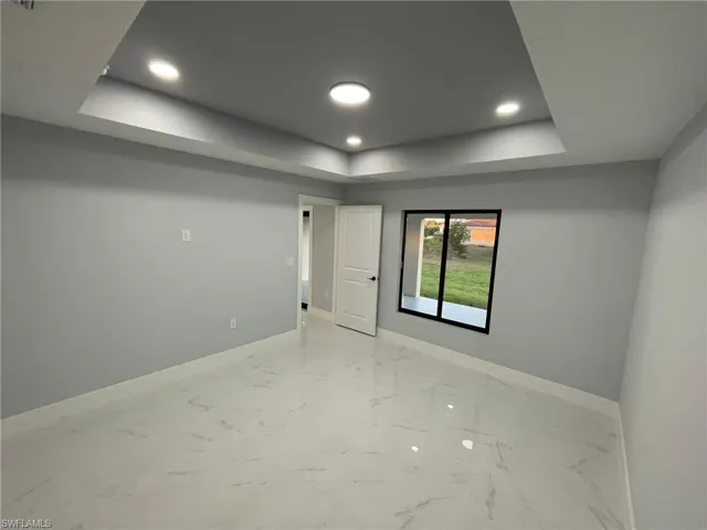 Unfurnished room featuring a raised ceiling, baseboards, recessed lighting, and light marble finish flooring