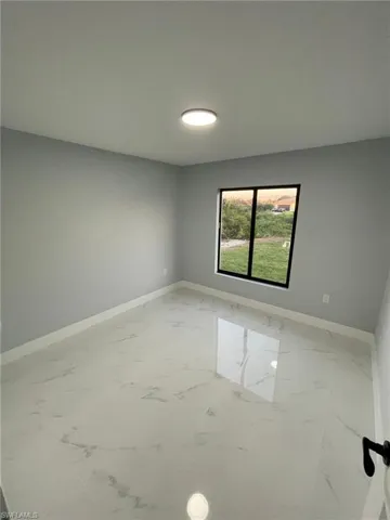 Empty room featuring marble look tiles and baseboards