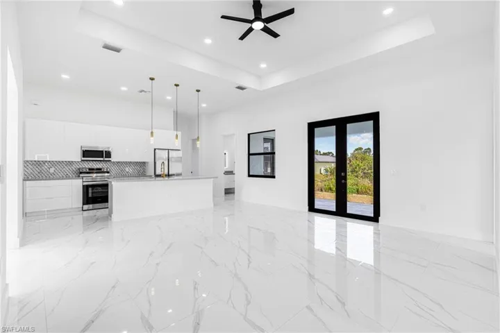 Unfurnished living room featuring ceiling fan, a raised ceiling, french doors, recessed lighting, and light marble finish flooring