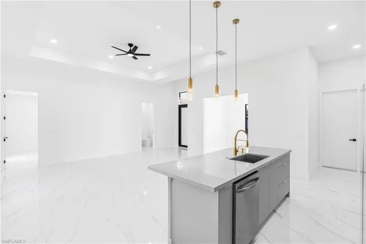 Kitchen featuring a center island with sink, pendant lighting, ceiling fan, light marble finish flooring, and stainless steel dishwasher