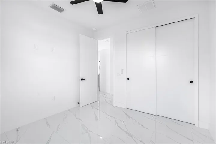 Unfurnished bedroom with light marble finish flooring, a ceiling fan, and a closet