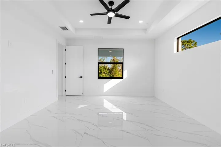 Empty room featuring plenty of natural light, a raised ceiling, a ceiling fan, light marble finish floors, and recessed lighting