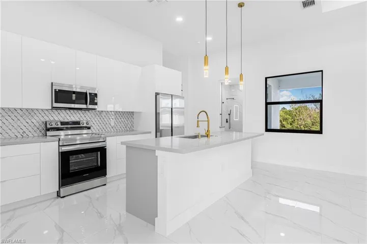 Kitchen with modern cabinets, stainless steel appliances, hanging light fixtures, white cabinets, and a center island with sink