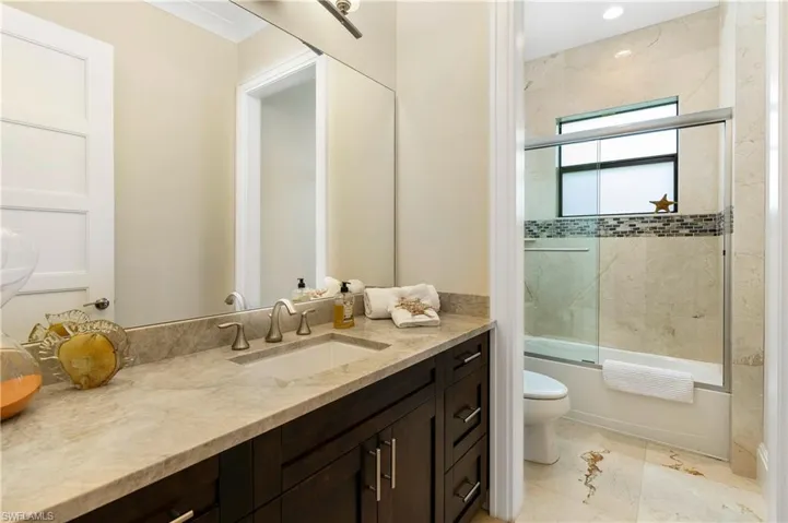 Full bathroom with toilet, bath / shower combo with glass door, and vanity