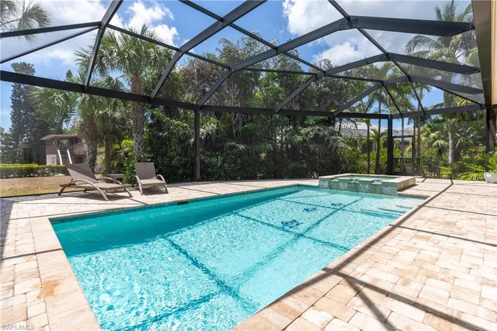 View of pool featuring a patio, glass enclosure, and a pool with connected hot tub