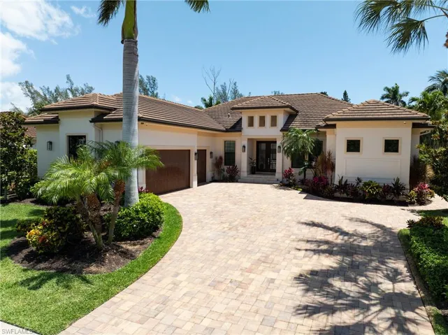 View of front facade with a tile roof, decorative driveway, an attached garage, and stucco siding