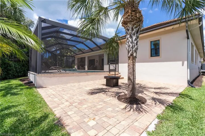 Back of property with an outdoor pool, a patio area, a lanai, stucco siding, and a yard