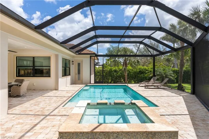 View of swimming pool with a patio, glass enclosure, and a pool with connected hot tub