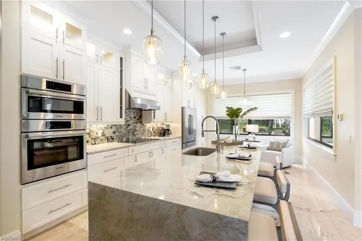 Kitchen featuring decorative backsplash, a sink, appliances with stainless steel finishes, a spacious island, and under cabinet range hood