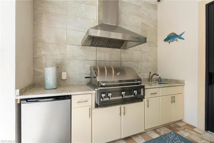 Kitchen with wall chimney range hood, tasteful backsplash, a sink, fridge, and light countertops