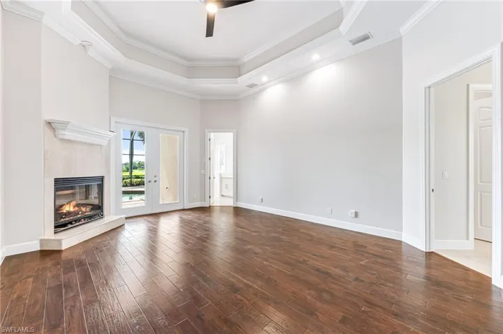 Unfurnished living room with dark wood finished floors, a high end fireplace, a ceiling fan, a tray ceiling, and crown molding