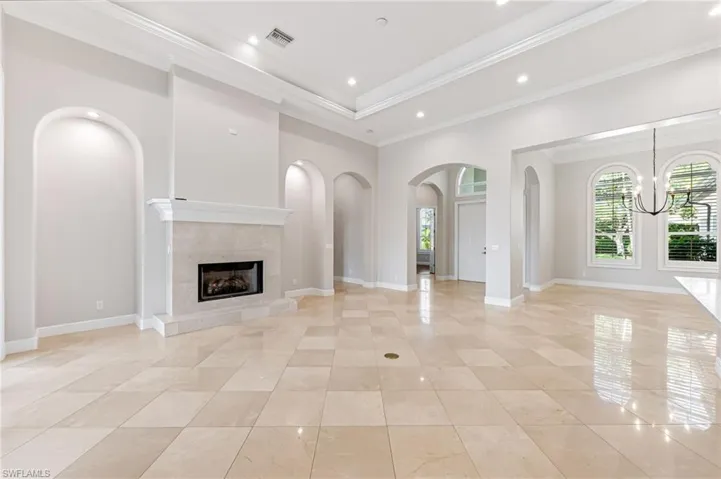 Unfurnished living room with a chandelier, a tiled fireplace, arched walkways, ornamental molding, and light tile patterned floors