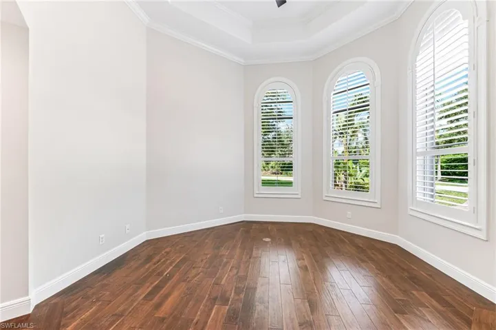 Empty room featuring a raised ceiling, dark wood finished floors, and ornamental molding