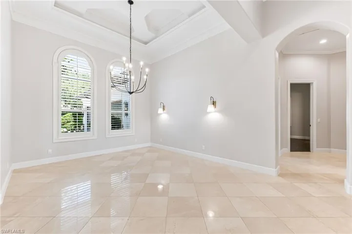 Unfurnished room featuring crown molding, arched walkways, light tile patterned flooring, a chandelier, and coffered ceiling