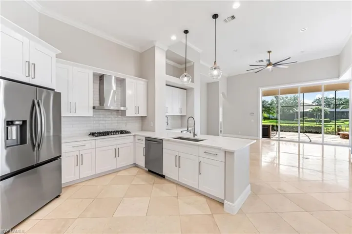 Kitchen with appliances with stainless steel finishes, wall chimney range hood, light tile patterned floors, a peninsula, and ornamental molding