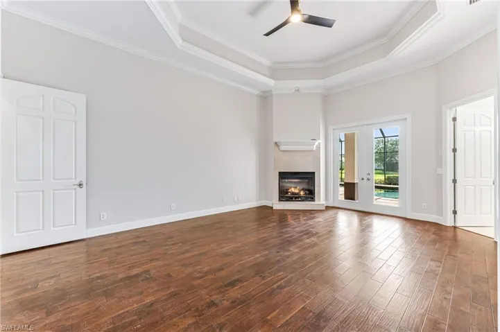 Unfurnished living room featuring dark wood-style floors, a tray ceiling, ceiling fan, a glass covered fireplace, and crown molding