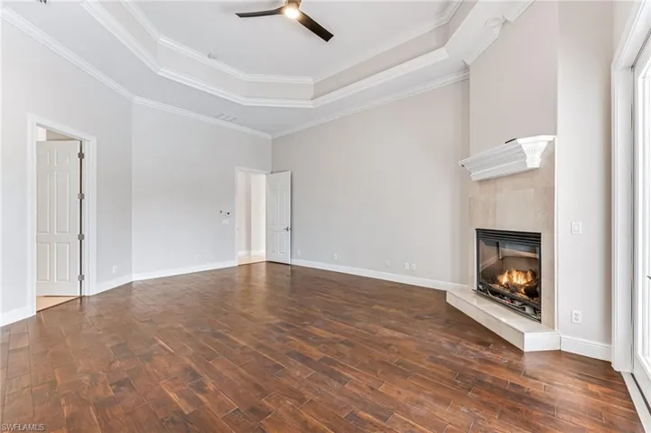 Unfurnished living room with a tray ceiling, a ceiling fan, dark wood-style floors, a tiled fireplace, and crown molding
