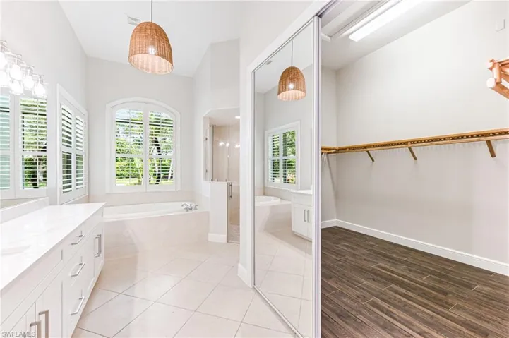Full bath featuring vanity, a garden tub, a stall shower, a spacious closet, and wood finished floors