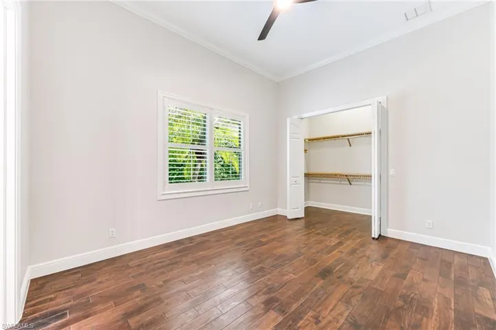Unfurnished bedroom with ornamental molding, dark wood finished floors, a ceiling fan, and a closet