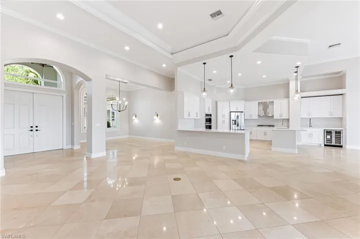 Unfurnished living room with wine cooler, arched walkways, light tile patterned floors, a chandelier, and crown molding