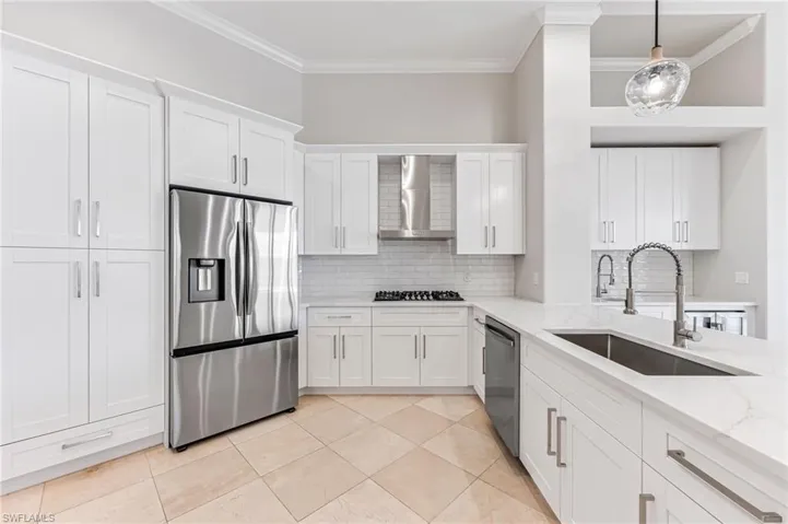 Kitchen with appliances with stainless steel finishes, wall chimney exhaust hood, ornamental molding, white cabinetry, and decorative backsplash
