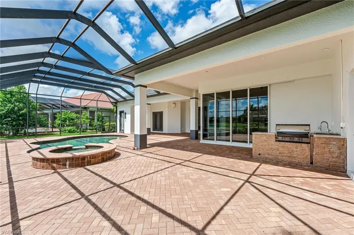 View of patio featuring exterior kitchen, glass enclosure, and a pool with connected hot tub