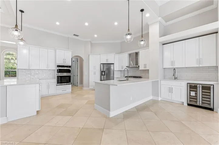 Kitchen with beverage cooler, appliances with stainless steel finishes, wall chimney range hood, crown molding, and decorative backsplash