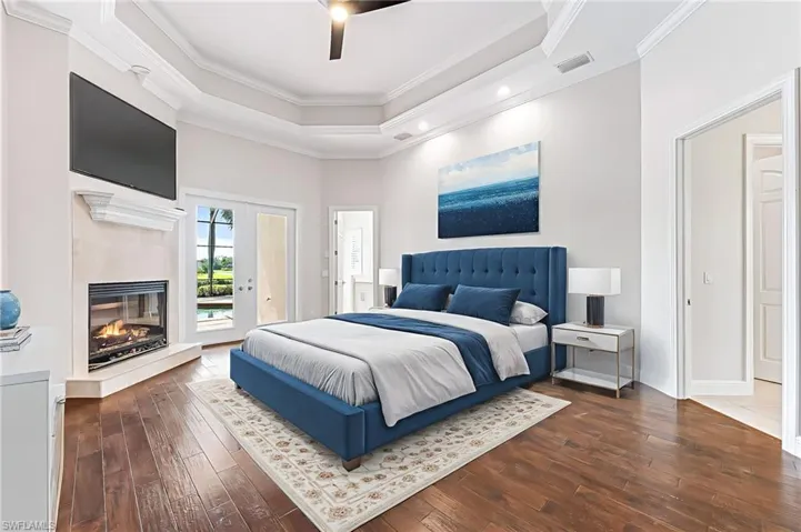 Bedroom with access to outside, dark wood-style floors, crown molding, a tray ceiling, and a multi sided fireplace