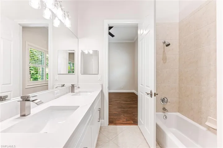 Full bath featuring double vanity, washtub / shower combination, ornamental molding, and tile patterned floors