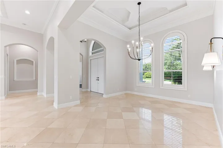 Empty room featuring arched walkways, ornamental molding, a chandelier, light tile patterned flooring, and coffered ceiling