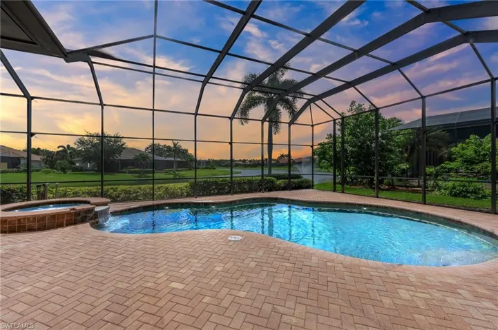 Pool at dusk with a pool with connected hot tub, glass enclosure, and a patio area