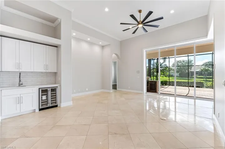 Unfurnished living room with wine cooler, arched walkways, crown molding, bar, and recessed lighting