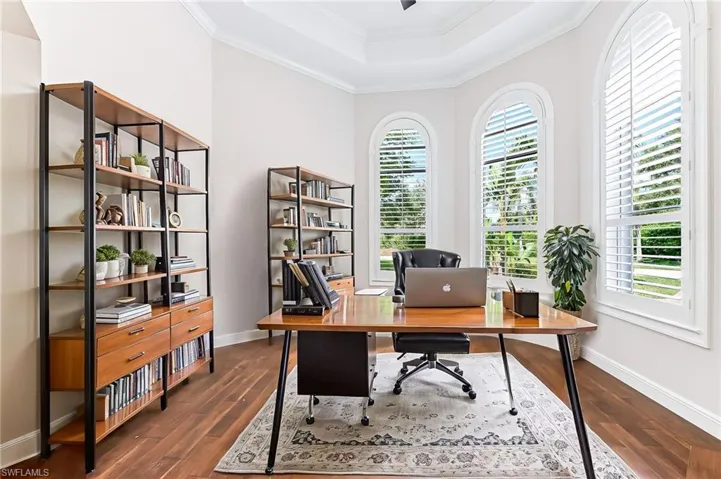 Home office with a tray ceiling, dark wood-style flooring, and crown molding