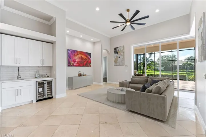 Living room with wine cooler, bar with sink, ornamental molding, arched walkways, and a ceiling fan