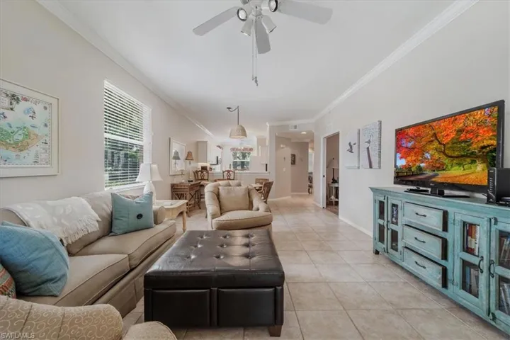 Living room featuring light tile patterned floors, ornamental molding, and a ceiling fan