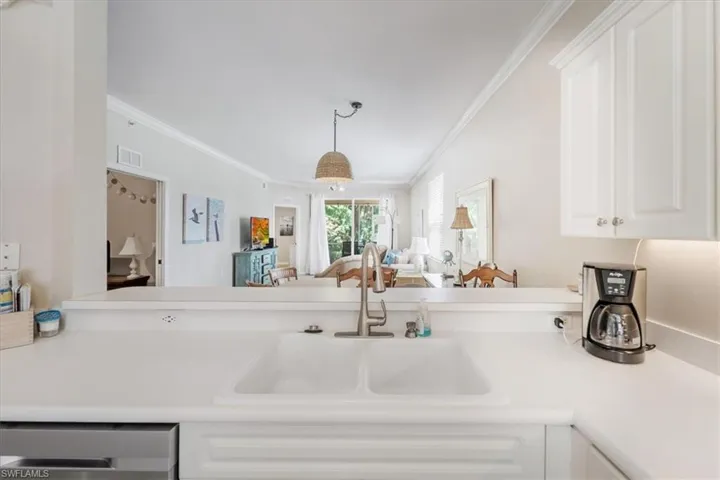 Kitchen with light countertops, open floor plan, white cabinetry, dishwasher, and crown molding