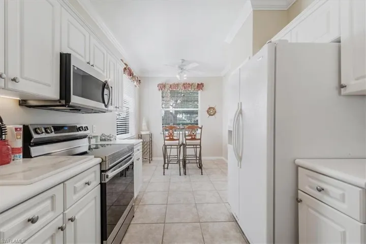Kitchen with stainless steel appliances, ornamental molding, white cabinetry, light countertops, and light tile patterned flooring