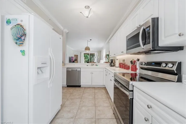 Kitchen featuring stainless steel appliances, crown molding, white cabinetry, light countertops, and light tile patterned flooring