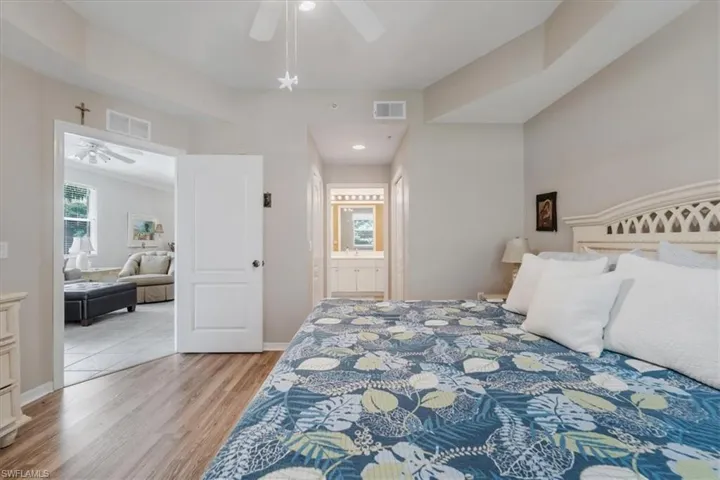 Bedroom with light wood-style flooring, ceiling fan, and ensuite bath